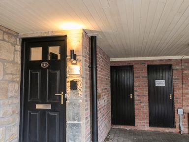 A black door with the number 1 and a light above next to two black doors in a brick and stone entrance at Lavenna Alnwick