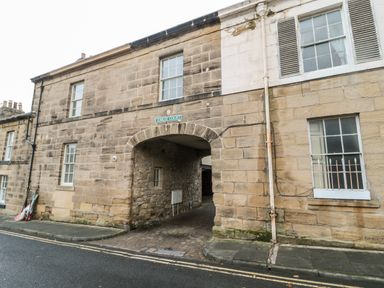 A stone building with an arched passageway and several windows at Jubilee Court in Alnwick