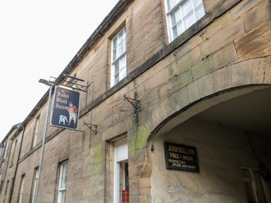 The exterior of a stone building with a sign for The John Bull Inn and an arched entrance at Lavenna in Alnwick