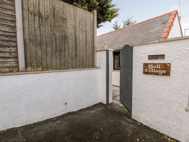 A white wall with a wooden gate and a sign reading Gull Cottage at Gull Cottage in Hermon near Newborough