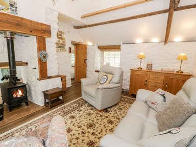 A living room with a wood stove armchairs a sofa wooden cabinet and a patterned rug at Gull Cottage in Hermon near Newborough
