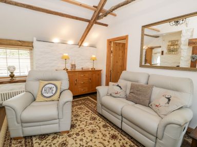 A living room with a leather armchair and sofa with pillows a wooden sideboard with lamps and a large mirror at Gull Cottage Hermon near Newborough
