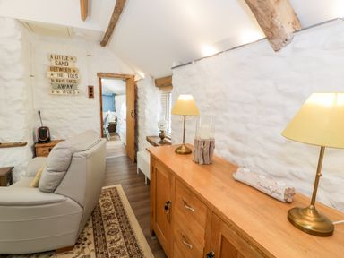 A living room with a beige sofa a wooden sideboard with two table lamps and a carpet on the floor at Gull Cottage in Hermon near Newborough