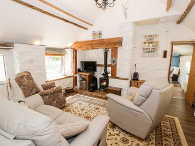 A living room with armchairs a rug a wood stove and a television at Gull Cottage in Hermon near Newborough