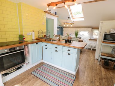 A kitchen with blue cabinets yellow tiled walls wooden countertops and a dining area with flowers at Gull Cottage in Hermon near Newborough