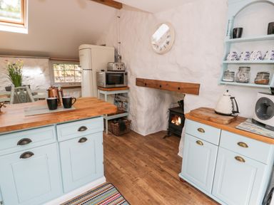 A kitchen with light blue cabinets wooden countertops a stove a microwave a refrigerator and a small dining table at Gull Cottage in Hermon near Newborough