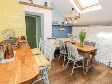 A kitchen with wooden countertops yellow tiled wall wooden dining table and light blue chairs at Gull Cottage in Hermon near Newborough