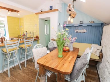 A kitchen and dining area with wooden table chairs and bar stools in a cottage at Gull Cottage Hermon near Newborough
