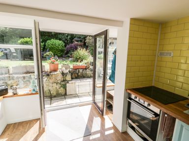 A kitchen with an oven a yellow tiled backsplash and an open door leading to a garden at Gull Cottage in Hermon near Newborough