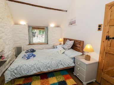 A bedroom with a bed and bedside tables with lamps and a window with curtains at Gull Cottage Hermon near Newborough