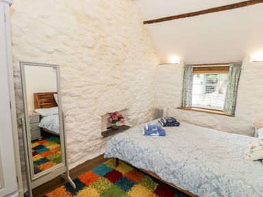 A bedroom with a bed covered in patterned bedding a full-length mirror and a colorful rug at Gull Cottage in Hermon near Newborough