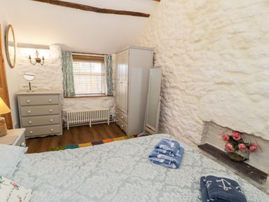 A bedroom with stone walls bed pillows towels dresser wardrobe and a window with curtains at Gull Cottage in Hermon near Newborough