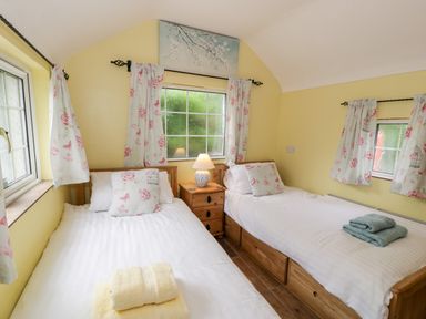 A bedroom with two single beds and floral curtains at Gull Cottage in Hermon near Newborough