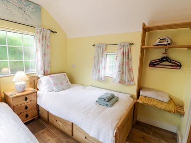A bedroom with two single beds a bedside table with a lamp wooden open wardrobe with hangers and an iron at Gull Cottage in Hermon near Newborough