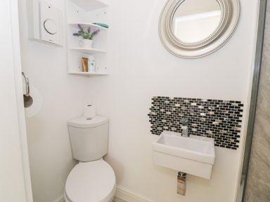 A small bathroom with a toilet a wall-mounted sink and a round mirror above the sink at Gull Cottage in Hermon near Newborough