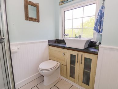 A bathroom with a toilet sink wooden cabinets and a window at Gull Cottage in Hermon near Newborough