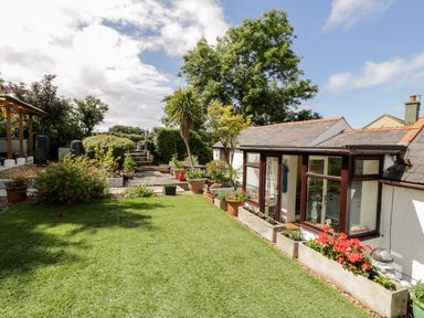 A garden with potted plants a lawn and a house with large windows at Gull Cottage in Hermon near Newborough
