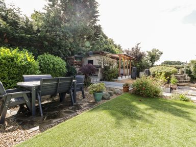 An outdoor garden area with a table and chairs next to a shed and greenery at Gull Cottage in Hermon near Newborough