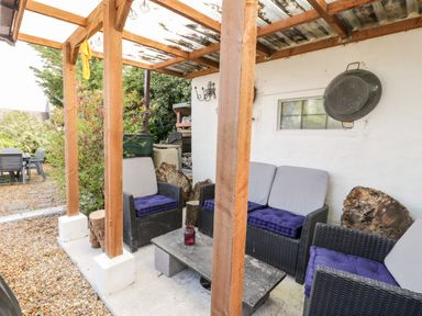 An outdoor seating area with wicker chairs and blue cushions under a wooden pergola at Gull Cottage in Hermon near Newborough
