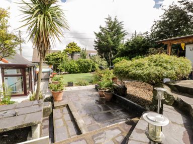 A garden with stone patio grass lawn potted plants and trees at Gull Cottage in Hermon near Newborough