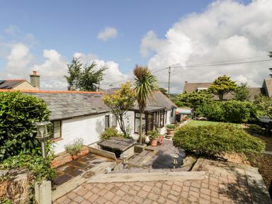 An outdoor patio area with stone paving plants and a white house with a tiled roof at Gull Cottage in Hermon near Newborough