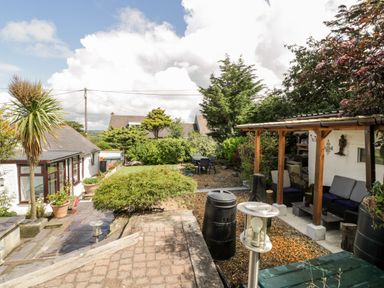 A garden with a patio seating area a tree and outdoor furniture at Gull Cottage in Hermon near Newborough