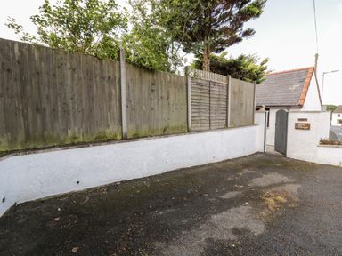 A paved driveway with a wooden fence and a gate leading to a white building at Gull Cottage in Hermon near Newborough