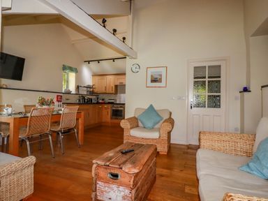 A living room and kitchen area with wicker chairs wooden table and a wooden chest at Abalone in Bude