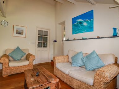 A living room with wicker armchairs and a sofa with blue cushions and a wooden coffee table at Abalone in Bude