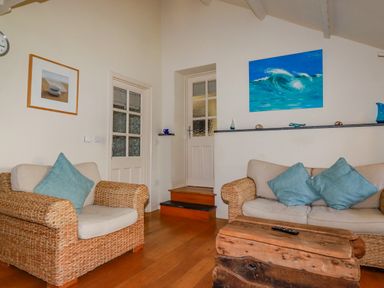 A living room with wicker armchairs with cushions wooden coffee table paintings on the walls at Abalone in Bude