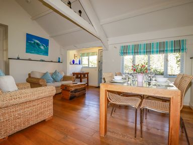 A dining and living area with a wooden table set with dishes and glasses and wicker sofas at Abalone in Bude