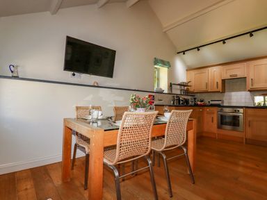 A kitchen with wooden cabinets and appliances and a dining table with four chairs and a TV on the wall at Abalone in Bude