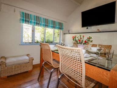 A dining area with a glass table set for four with woven chairs and a television on the wall at Abalone in Bude