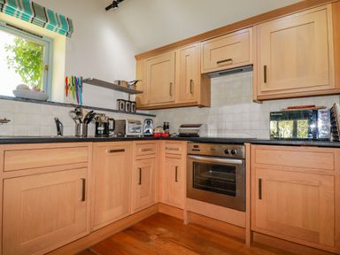 A kitchen with wooden cabinets an oven toaster microwave and a window at Abalone in Bude