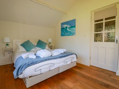 A bedroom with a double bed two pillows two bedside tables with lamps a painting of a wave and a door at Abalone in Bude