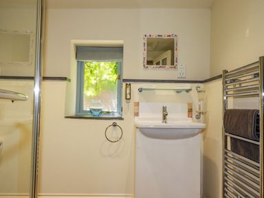 A bathroom with a shower enclosure a sink a small window with a vase on the sill a towel ring and a chrome heated towel rail with towels at Abalone in Bude