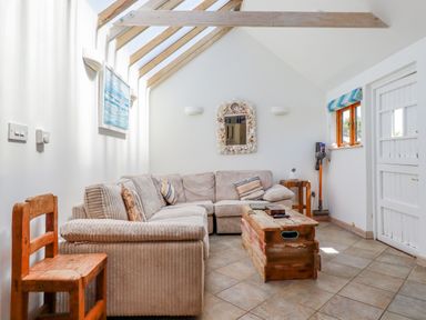 A living room with a beige sectional sofa wooden coffee table and chair under a skylight at Seashells Atlantic Highway near Bude