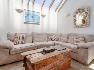 A living room with a beige corner sofa and wooden coffee table with a mirror framed with shells at Seashells Atlantic Highway near Bude