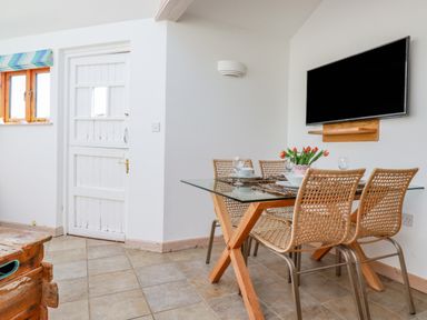 A dining area with a glass table and wicker chairs a white door and a wall mounted television at Seashells Atlantic Highway near Bude