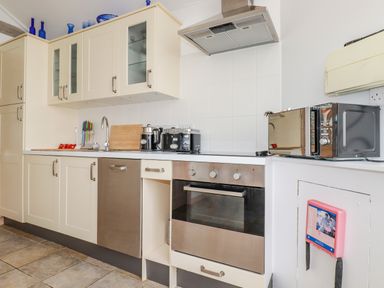 A kitchen with white cabinets a sink a toaster an oven and a microwave at Seashells in Atlantic Highway near Bude