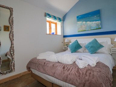 A bedroom with a double bed with blue pillows and folded towels on a blanket at Seashells Atlantic Highway near Bude