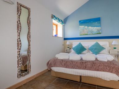 A bedroom with a bed with blue pillows and white towels a beach painting on the wall and a tall mirror at Seashells Atlantic Highway near Bude