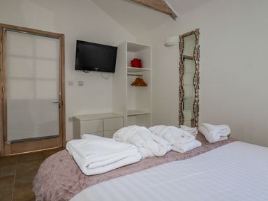 A bedroom with a bed that has towels and robes on it a wall-mounted tv a cabinet an open wardrobe and a tall mirror at Seashells Atlantic Highway near Bude