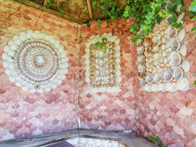 A corner wooden bench with walls decorated in patterns of various seashells and green ivy at Seashells Atlantic Highway near Bude