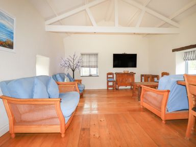 A living room with wooden sofas with blue cushions a coffee table a TV on the wall and wooden floor at Oyster Atlantic Highway near Bude