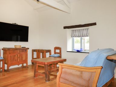 A sitting room with wooden furniture a mounted TV and a window with striped blinds at Oyster Atlantic Highway near Bude