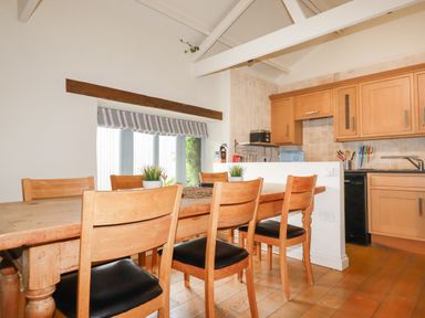 A dining area with a wooden table and chairs next to a kitchen with wooden cabinets at Oyster Atlantic Highway near Bude