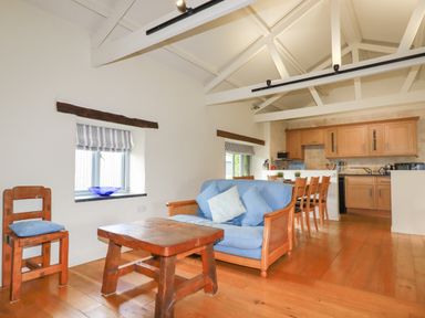 An open living room and kitchen with wooden furniture a blue sofa and exposed ceiling beams at Oyster Atlantic Highway near Bude