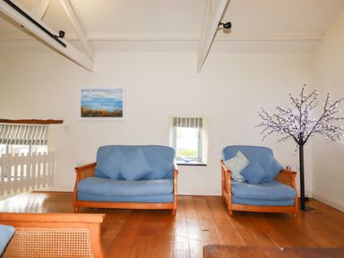 A living area with two blue cushioned wooden sofas a window with a striped blind a painting on the wall and a decorative light tree at Oyster Atlantic Highway near Bude