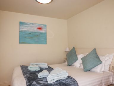 A bedroom with a bed with pillows and folded towels on a blanket and a painting on the wall at Oyster Atlantic Highway near Bude